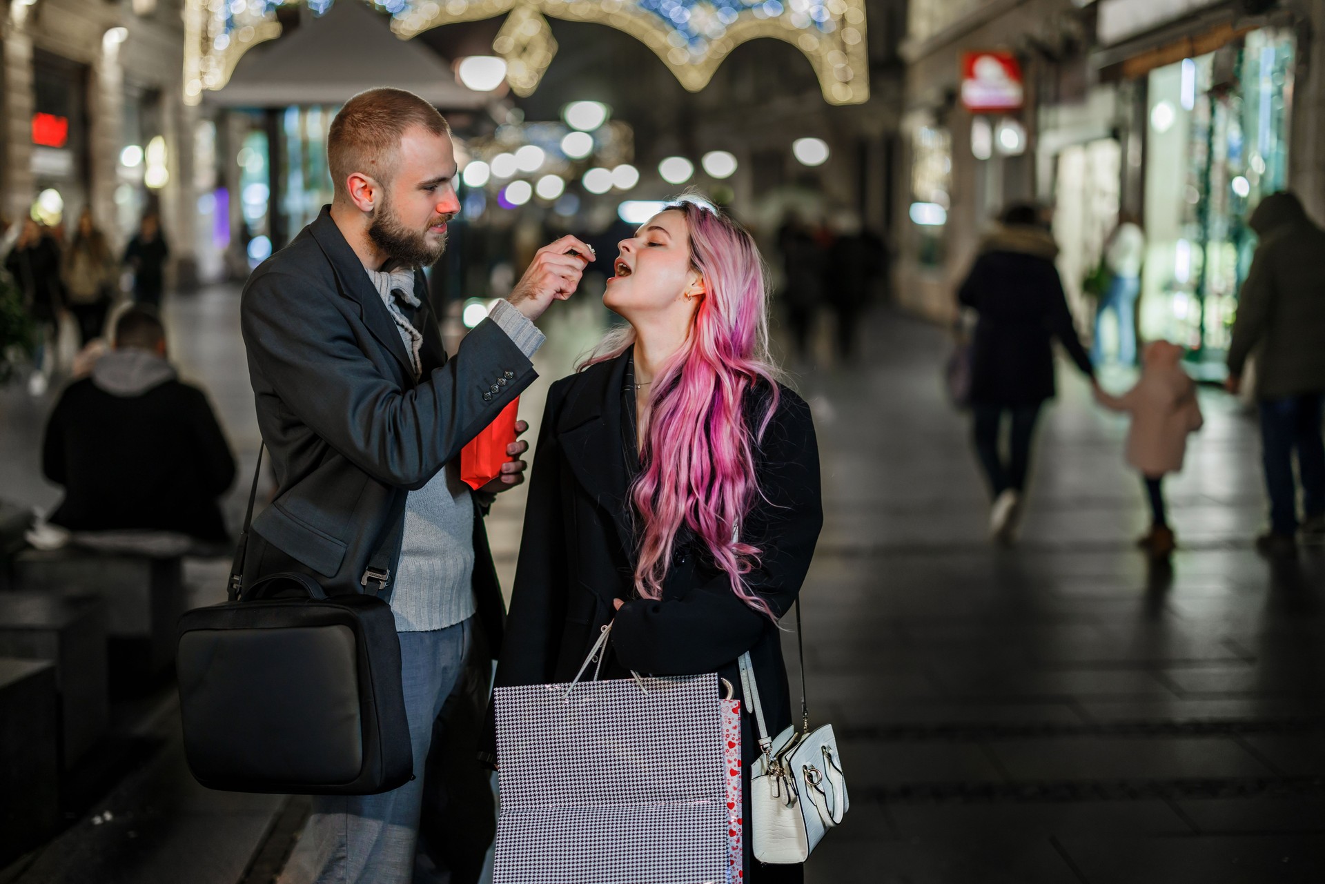 A fashionable young couple is enjoying in city walk on a cold night and eating popcorn.