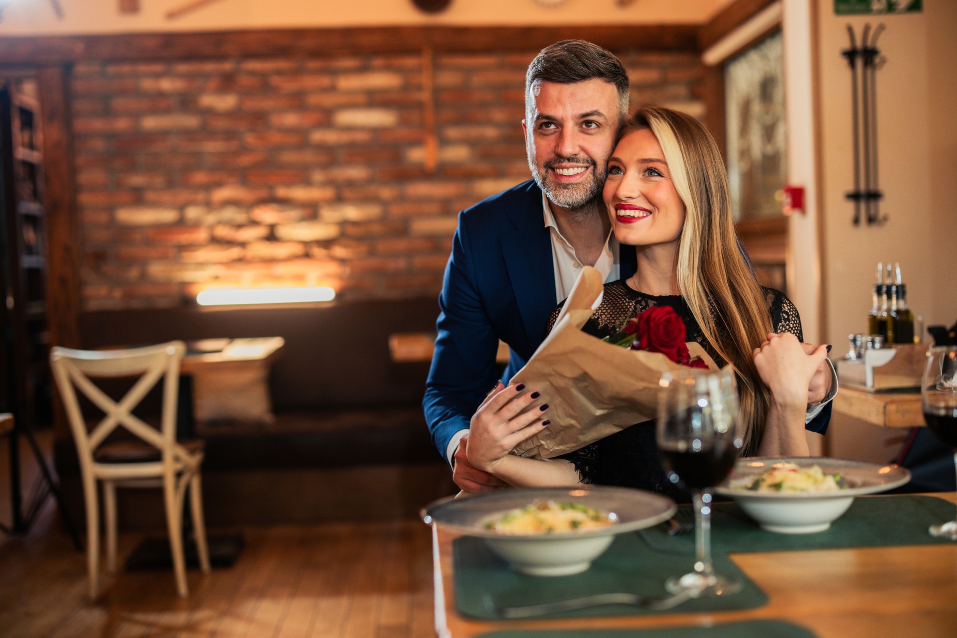 Portrait of a lovely couple enjoying a romantic dinner with red roses, fine wine and savory food